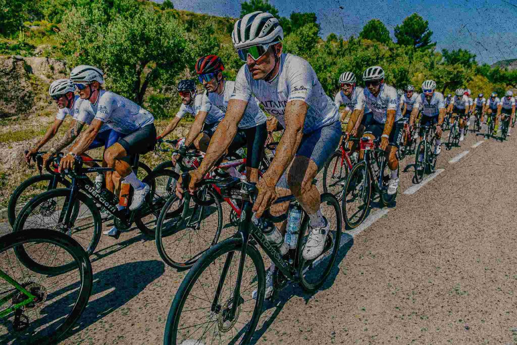 Syklister i Aitana Tour-trøyer på rekke langs en landevei
