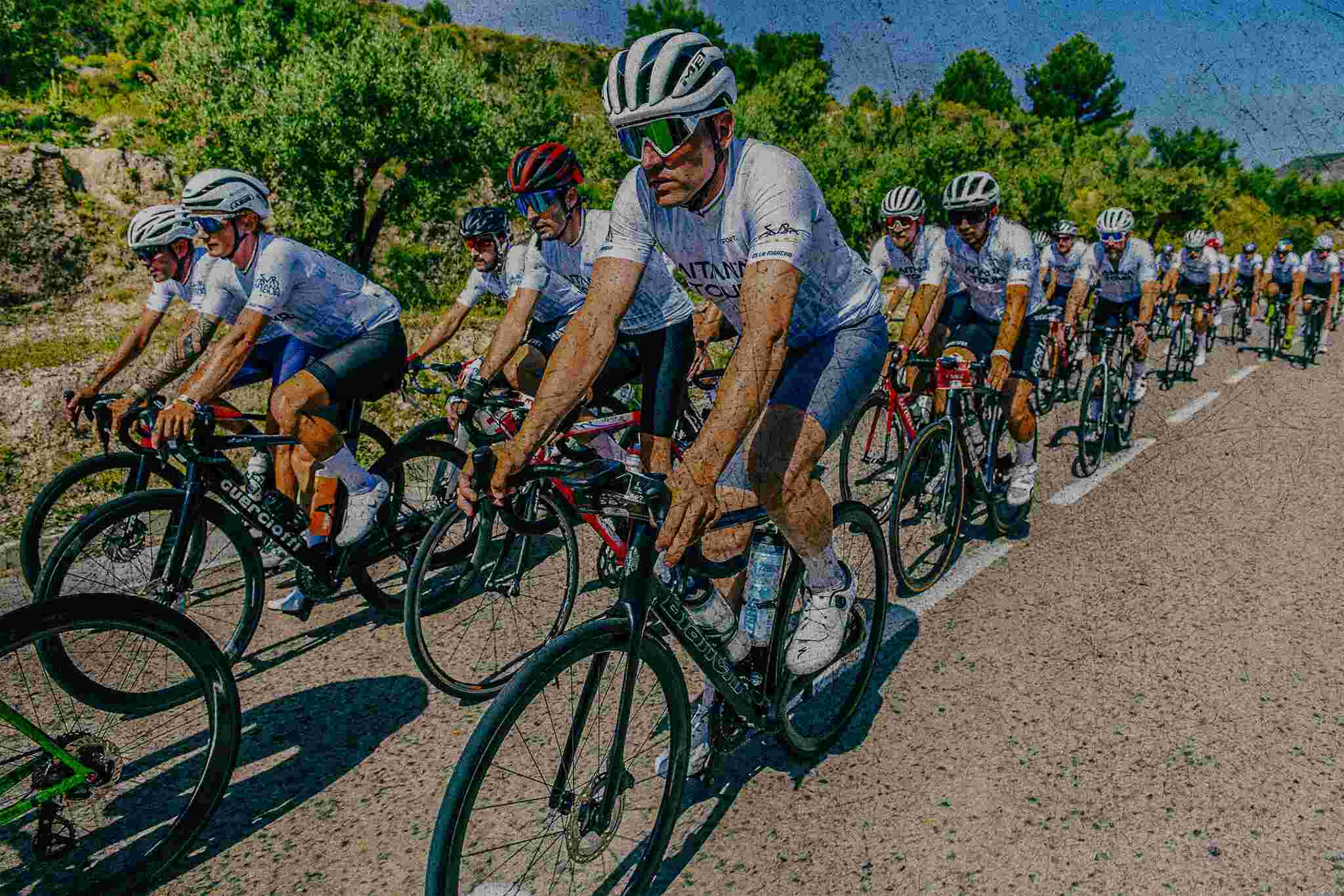 Syklister i Aitana Tour-trøyer på rekke langs en landevei